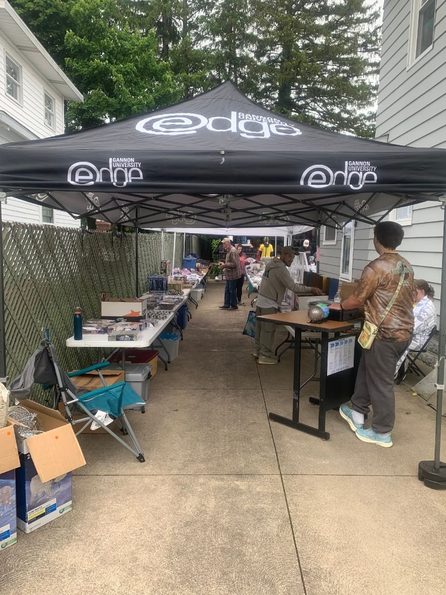 Shoppers browsing tables under a canopy on a wet sale day