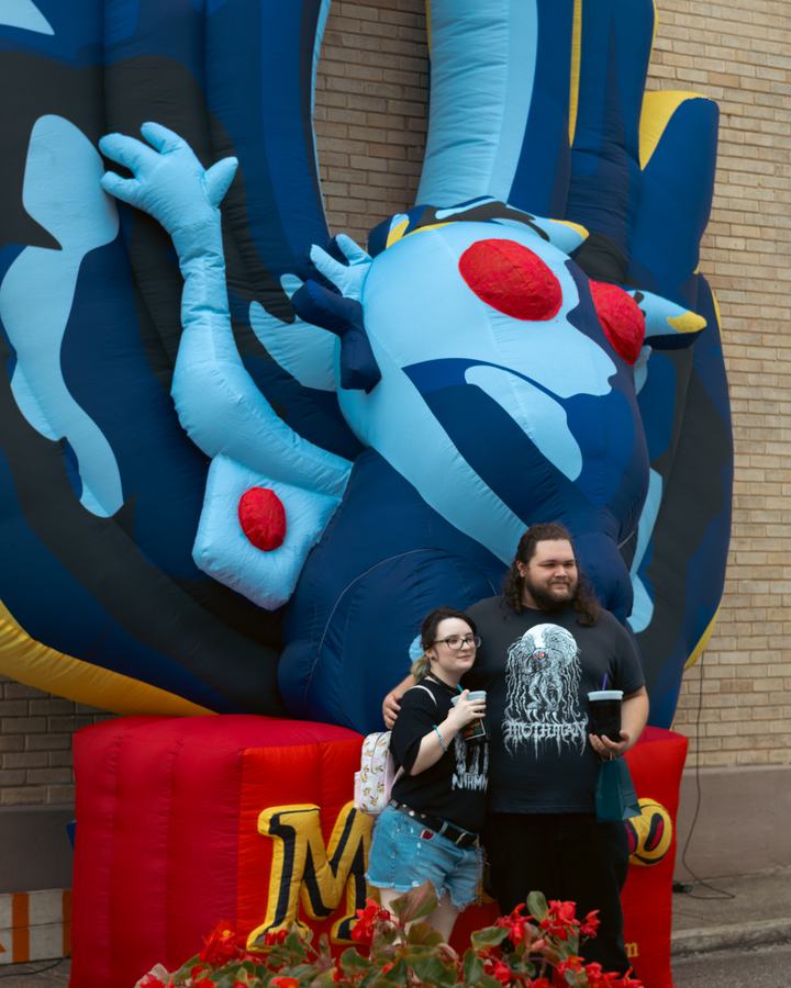 A couple posing before an inflatable Mothman at the MetaZoo booth