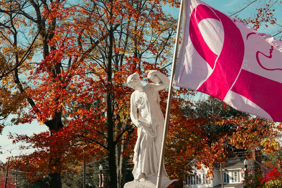 A white statue and a pink ribbon flag among red maples